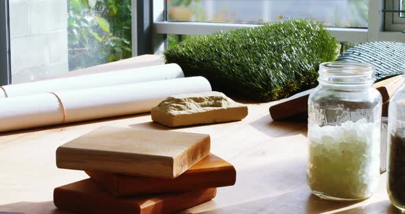 Sample of pebbles in jar, slab, blueprint and artificial turf on table alt