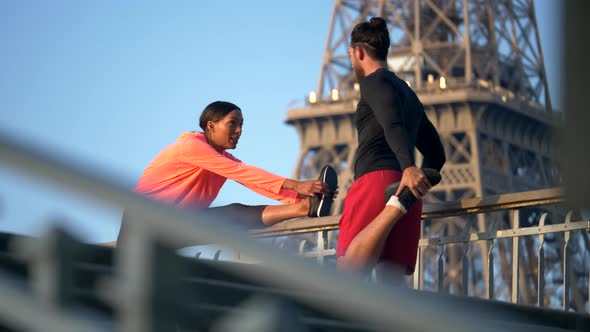 A couple stretching before running across a bridge with the Eiffel Tower alt