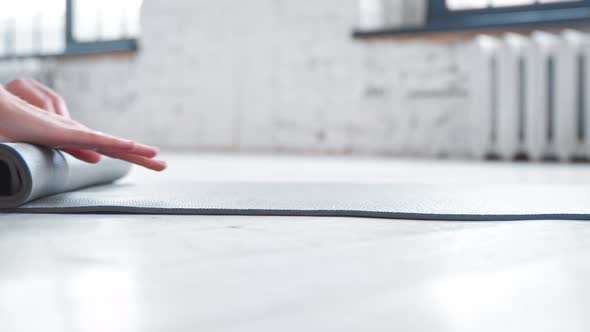Lady hands roll grey rubber mat after training on parquet floor in spacious light yoga studio alt