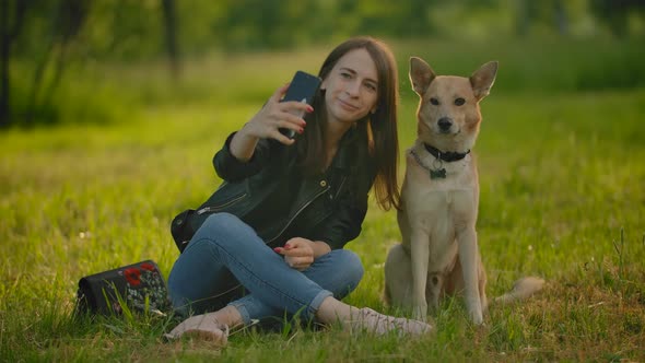 Girl Makes Selfie on a Smartphone Next To Her Dog. alt