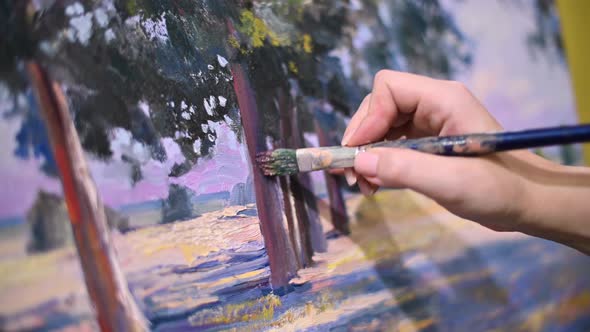 The artist s hand with a brush glides over the canvas of the painting alt