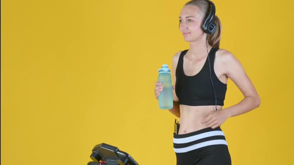 girl in sportswear with headphones works out on a treadmill