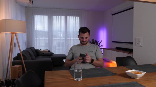 Man sits at a table in the living room and controls the lighting using a smartphone app - Smarthome alt