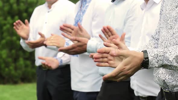 A group of men in white shirts applauds outdoors.  Clapping hands close up .