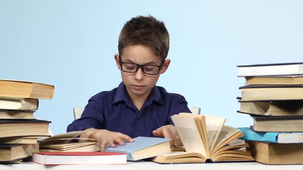 Boy Sits at the Table and Pull Up a Page with a Notebook. Blue Background. alt