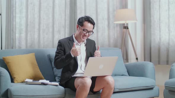 Asian Businessman In Jacket And Shorts Showing Thumbs Up Gesture While Having Video Call On A Laptop alt