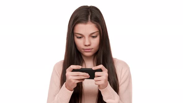 Portrait of Tense Concentrated Female Teenager with Very Long Brown Hair Playing Game on Her Cell alt