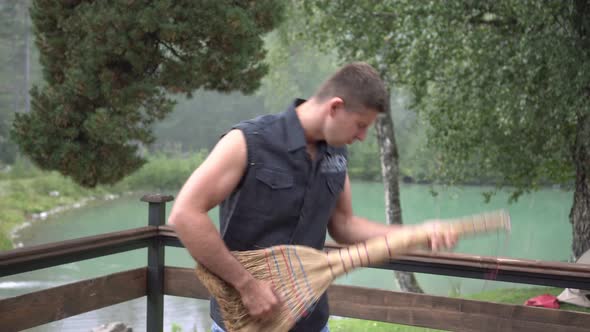 A Male Guitarist Holds a Broom Like a Guitar and Shows That He is Playing Music alt