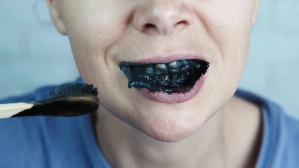 A woman brushes her teeth with activated charcoal.  alt
