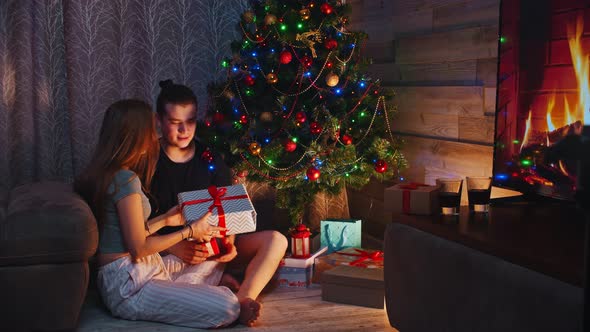Young Couple Sitting on the Floor Near the Tree and Exchanging Gifts on Christmas alt