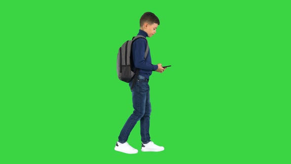 Schoolboy with a Backpack Using Mobile Phone While Walking on a Green Screen, Chroma Key alt