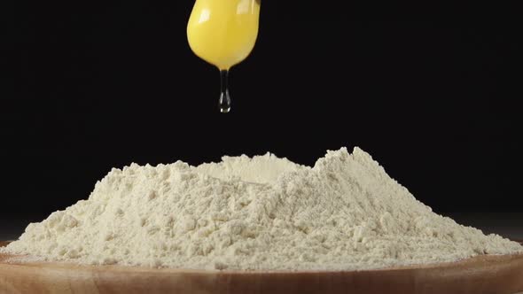 Egg Falls On A Pile Of Flour On A Black Background alt