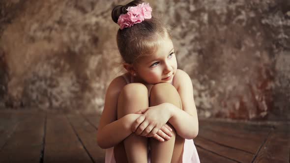 Sad Little Cute Baby Girl with Bows on Her Head Sitting on the Floor Crosslegged alt