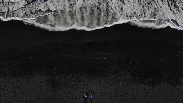 Aerial View of a Two People Sitting on the Beach with Black Sand.