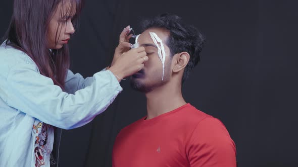 Make up artist putting white prosthetic insert on man's face to make a Halloween mask alt
