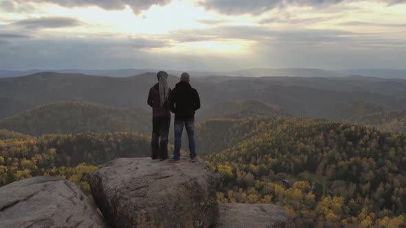 A Young Couple Stand on Top of a Mountain and Enjoy the Sunset. Hikers on a High Cliff.
