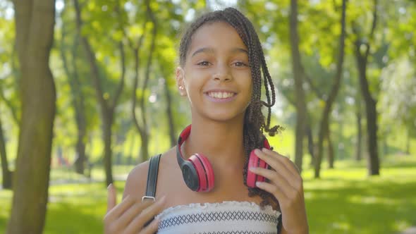 Close-up Portrait of Charming Happy Girl with Afro Pigtails and Brown Eyes Taking Off Headphones and alt