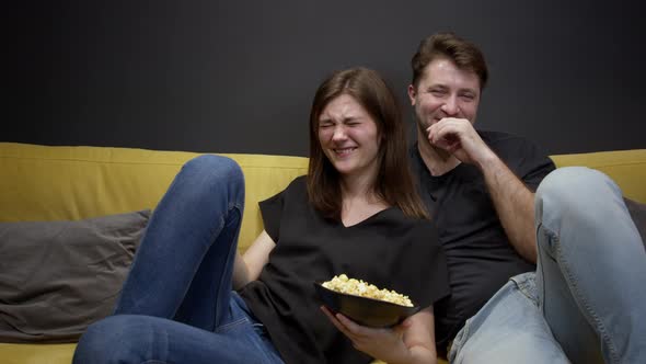 Attractive Young Couple Sitting on Sofa with Popcorn Watching Movie on TV