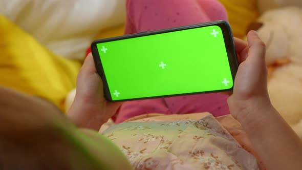 Green Screen on a Smartphone in the Hands of a Preschool Girl alt
