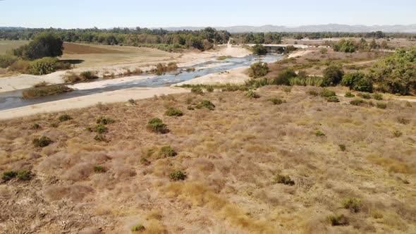 Aerial fly over of desert land and plants cut through by a rocky creek. alt