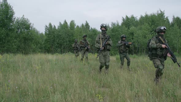 Soldiers in Camouflage with Assault Rifle Walking Through the Field Military Action in the Steppe alt