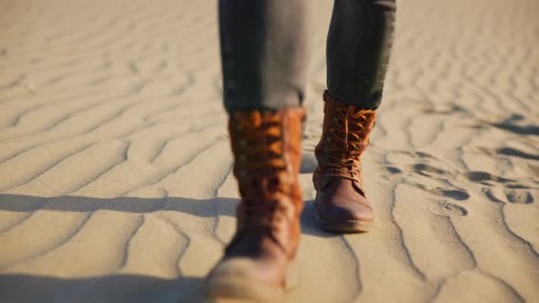Woman's feet in boots walking on the sand in the desert alt