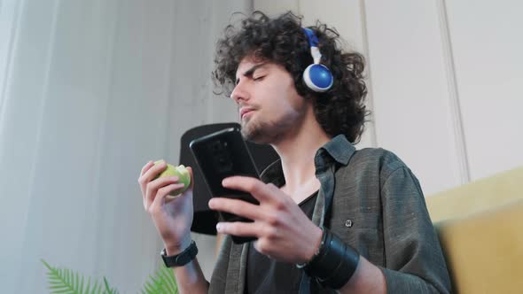Young Man Listening to the Music and Gesturing While Eatting an Apple alt