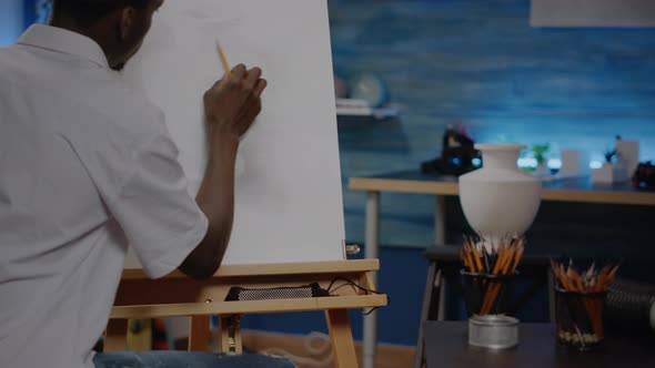Black Young Artist Retouching Vase Design on Canvas and Easel alt