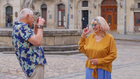 Elderly Tourist Grandfather Taking Photo Pictures of Grandmother on Retro Camera in Old Summer Town alt