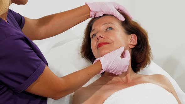 Aged Woman Smiling While Cosmetologist Examining Her Face alt