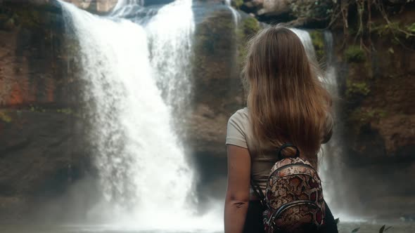 Female Backpacker Tourist Looking at Waterfall in Jungles Touches Her Long Hair alt