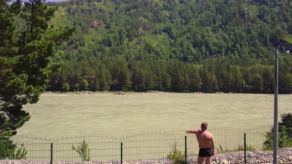 Aerial Flying Over a Mountain River with a Rapid Current A Man Dressed in Panties Looks at the River alt