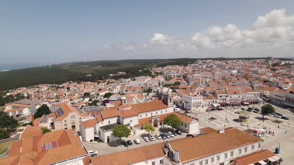 Aerial ascending Sanctuary of Nossa Senhora da Nazaré on the hilltop, rooftops on Cityscape alt
