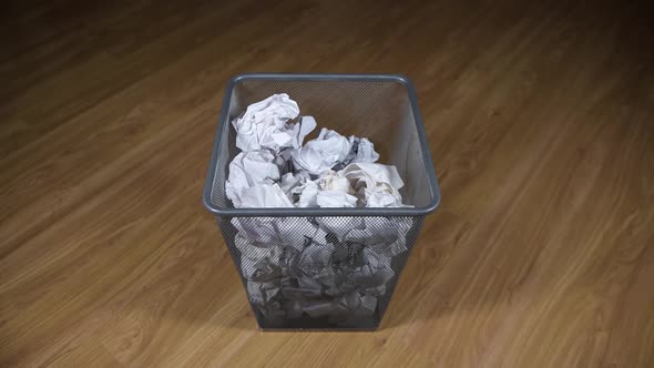 the trash paper basket is on the floor and crumpled papers fly into the basket alt