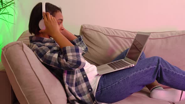 Young Woman Lying on the Couch with a Laptop Listening to Music