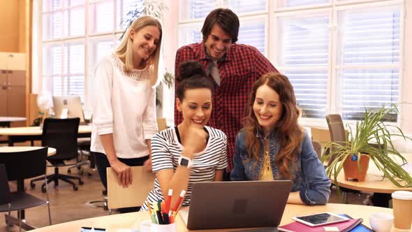 Group of business executives discussing over laptop at their desk alt