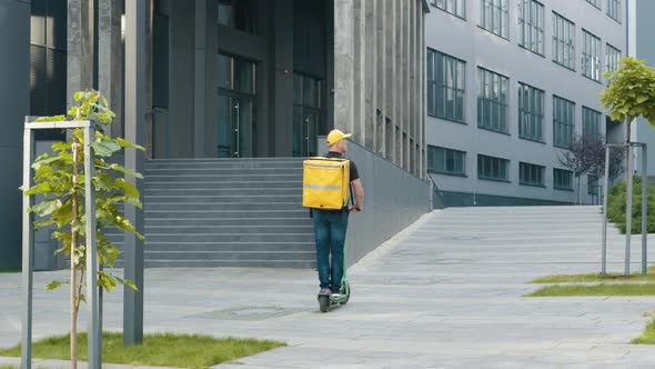 Delivery Man with Yellow Backpack Rides a Electric Scooter Through the City with alt