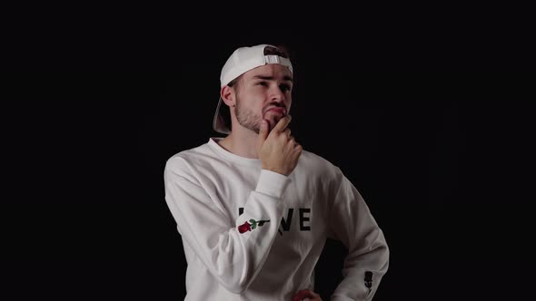 Trendy 20s Man rubbing chin and thinking, wide, black background alt