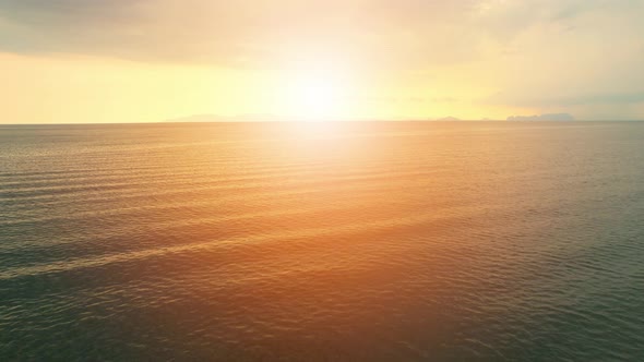 An aerial view of a drone flying over sea waves during sunrise alt