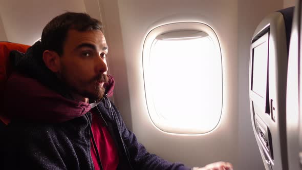 Bearded Young Man is Sitting Inside of a Plane Next to the Window When Somebody Makes Him Wear Mask alt
