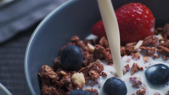Pouring Natural Organic Milk or Yogurt Into Ceramic Bowl with Healthy Granola and Mix of Fresh alt
