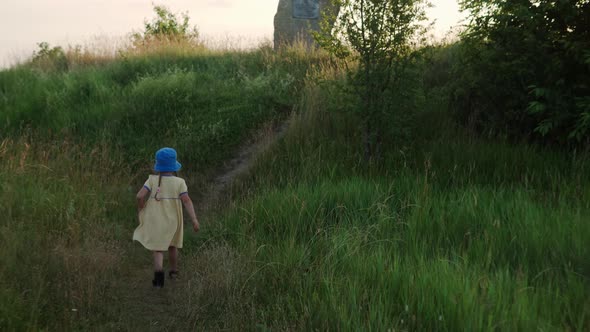 Cute Preschool Little Baby Girl in Yellow Dress Climbing Up Trail in Tall Grass Before Sunset alt