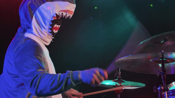 Side View of Musician in a Festive Shark Costume Plays Drums and Hits Percussion Cymbals alt