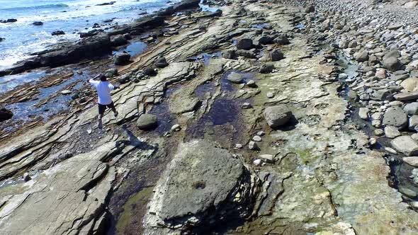 Tracking shot of a young man running on a rocky ocean beach shoreline alt