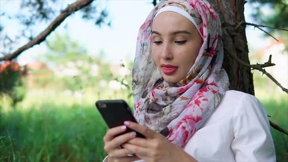 A Woman with a Hijab Chatting with Friends on a Smartphone a Lady Is in the Park alt