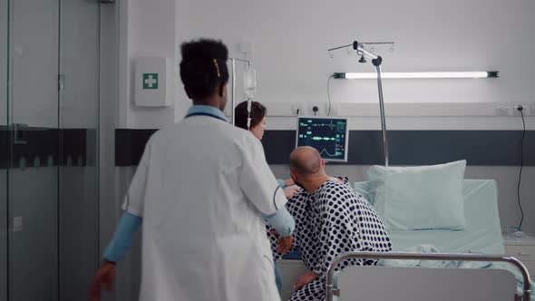 Physician Doctors Helping Patient to Stand Up From Bed Holding Intravenous IV Fluid Drip Bag alt