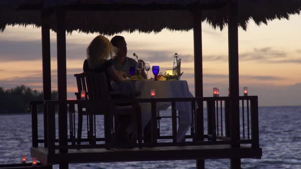 A man and woman couple eat dinner and dine in a hut on a tropical island beach alt