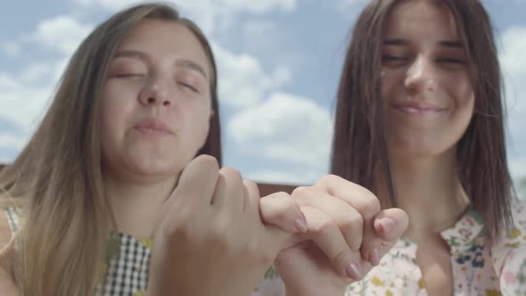 Attractive Girls Taking Each Other's Little Fingers and Smiling, Looking in the Camera alt