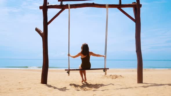 A Young Woman in Green Swimming Suit Swinging on a Swings on the Clean Beach alt