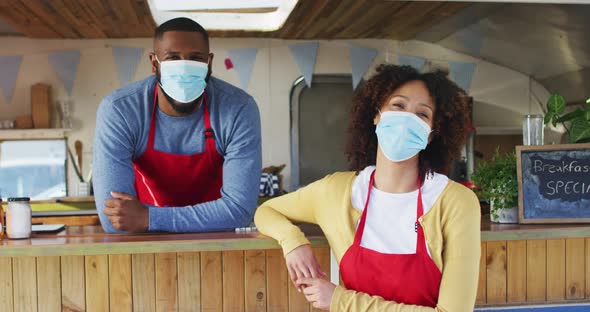 Portrait of african american couple wearing face masks standing near the food truck alt